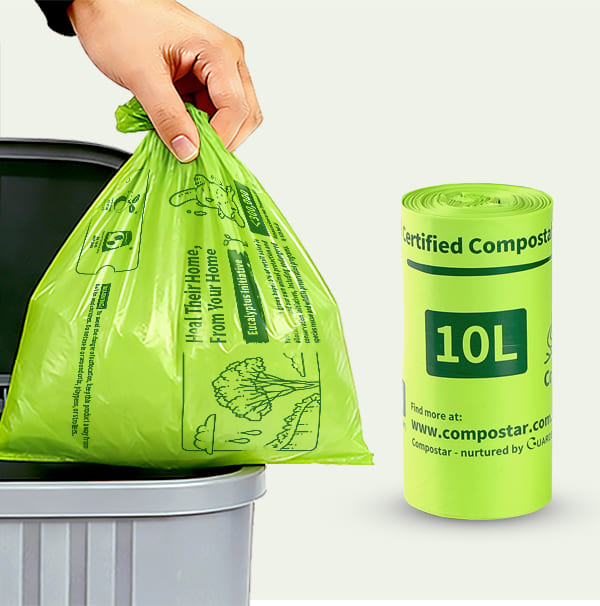 A hand lifting a full Compostar 10L certified compostable bin liner from a kitchen bin, shown next to a green roll of 10L FOGO bags.